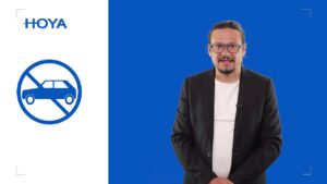 Mężczyzna w garniturze, po lewej znak zakazu z samochodem, tło niebieskie, logo Hoya, kontekst krótkowzroczność u dzieci.
