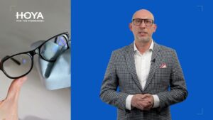 Mężczyzna w okularach i marynarce, obok okulary na ściereczce z logo HOYA, kontekst: wady wzroku u dzieci