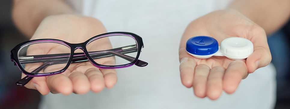 Osoba trzyma okulary i pojemnik na soczewki kontaktowe, symbolizujące wybór korekcji wzroku dla dzieci.