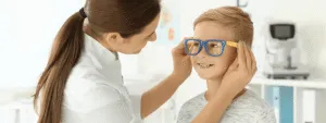 Optometrystka zakłada okulary na nos chłopca w gabinecie okulistycznym.